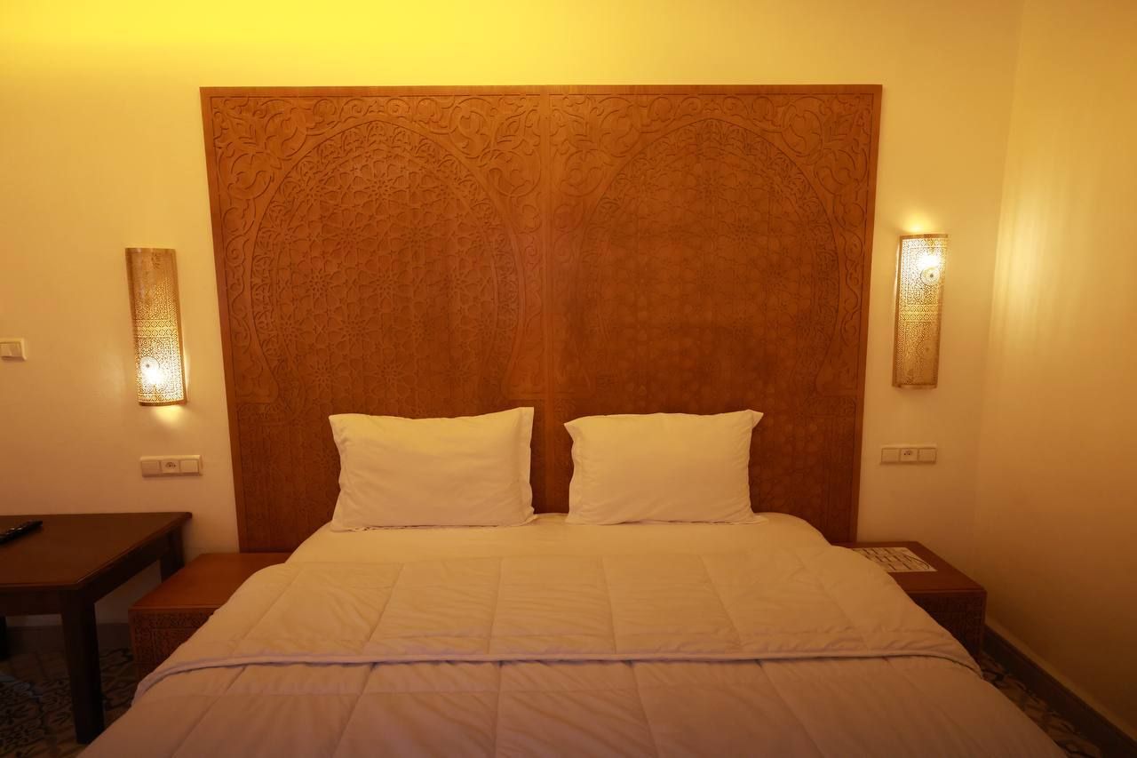 A hotel room with a large bed, two bedside tables, and a wooden headboard with intricate carvings.