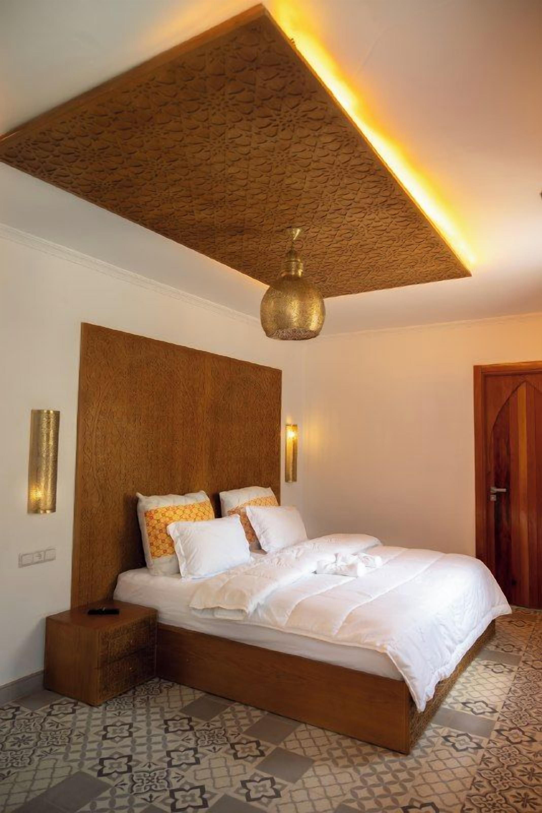 A bedroom with a large bed, a wooden headboard, a patterned floor, and a textured ceiling.