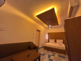 Una habitación de hotel con cama, sofá, una mesita y una lámpara en el techo.