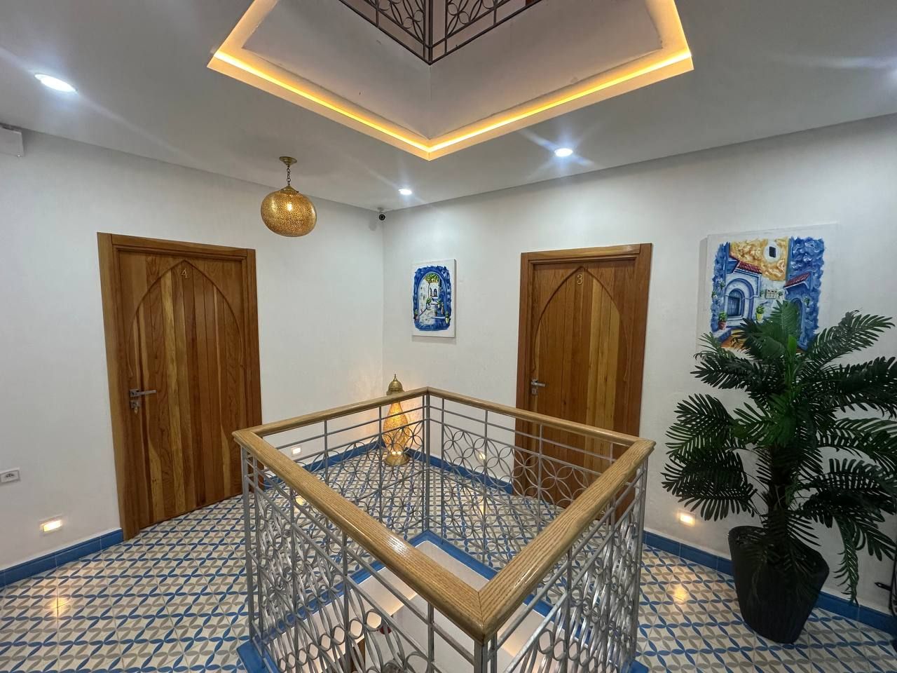 A room with a central glass table, wooden doors, a potted plant, and patterned floor tiles.