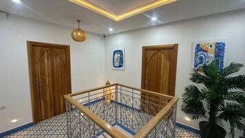 A room with a central glass table, wooden doors, a potted plant, and patterned floor tiles.