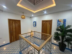 A room with a central glass table, wooden doors, a potted plant, and patterned floor tiles. - Diyar Marhaba (Chefchaouen)