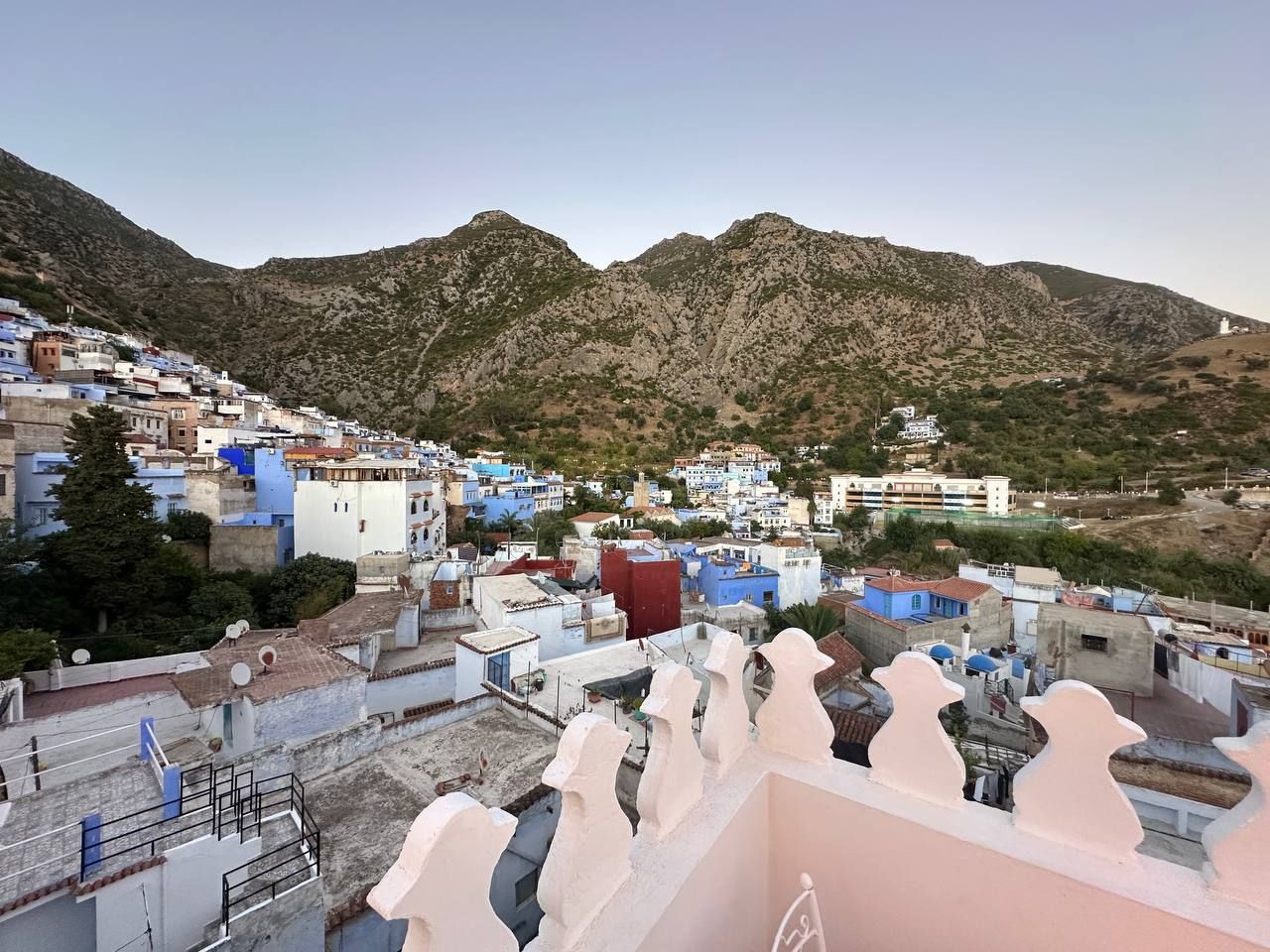Un pueblo montañoso con edificios de varios colores, una estructura blanca destacada en primer plano, y una mezquita con cúpula.