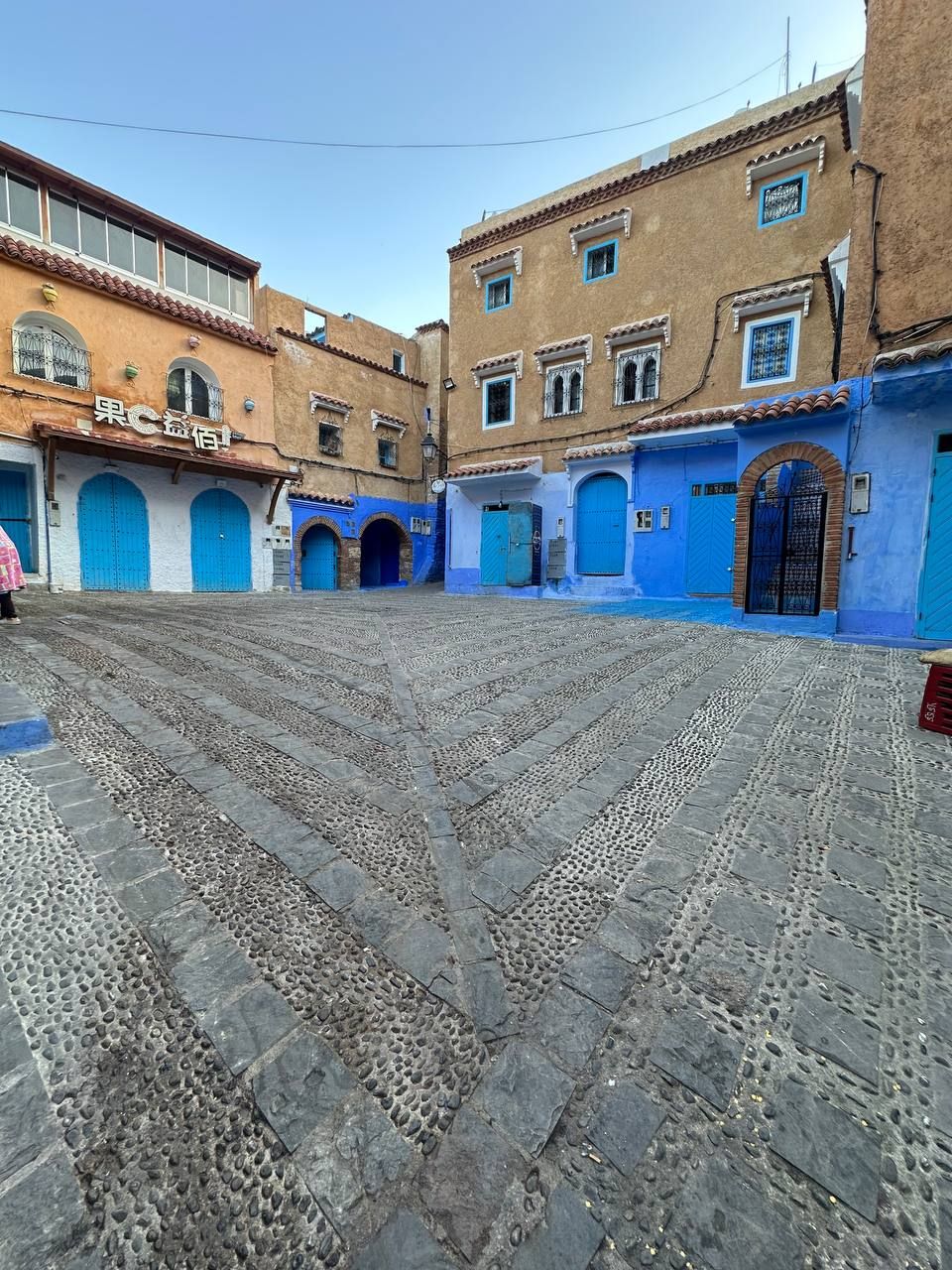 A courtyard with cobblestone flooring, blue doors, and buildings with traditional architecture.
