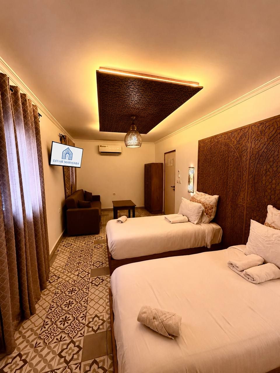 Une chambre d’hôtel avec deux lits, une télévision, une armoire et un revêtement de sol à motifs.