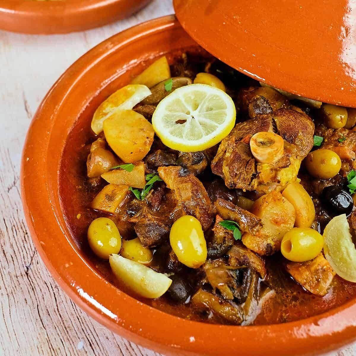 Una tradizionale pentola di terracotta colma di stufato, guarnita con limone e olive.