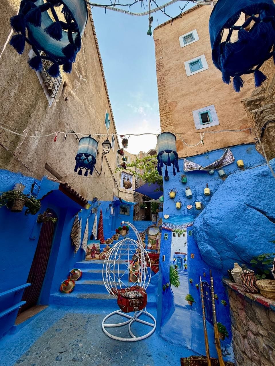 Un estrecho callejón con paredes azules, un sillón colgante y faroles tradicionales marroquíes.