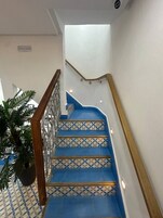 Una escalera con escalones de patrón azulado, barandillas de madera y una planta en maceta a la izquierda.