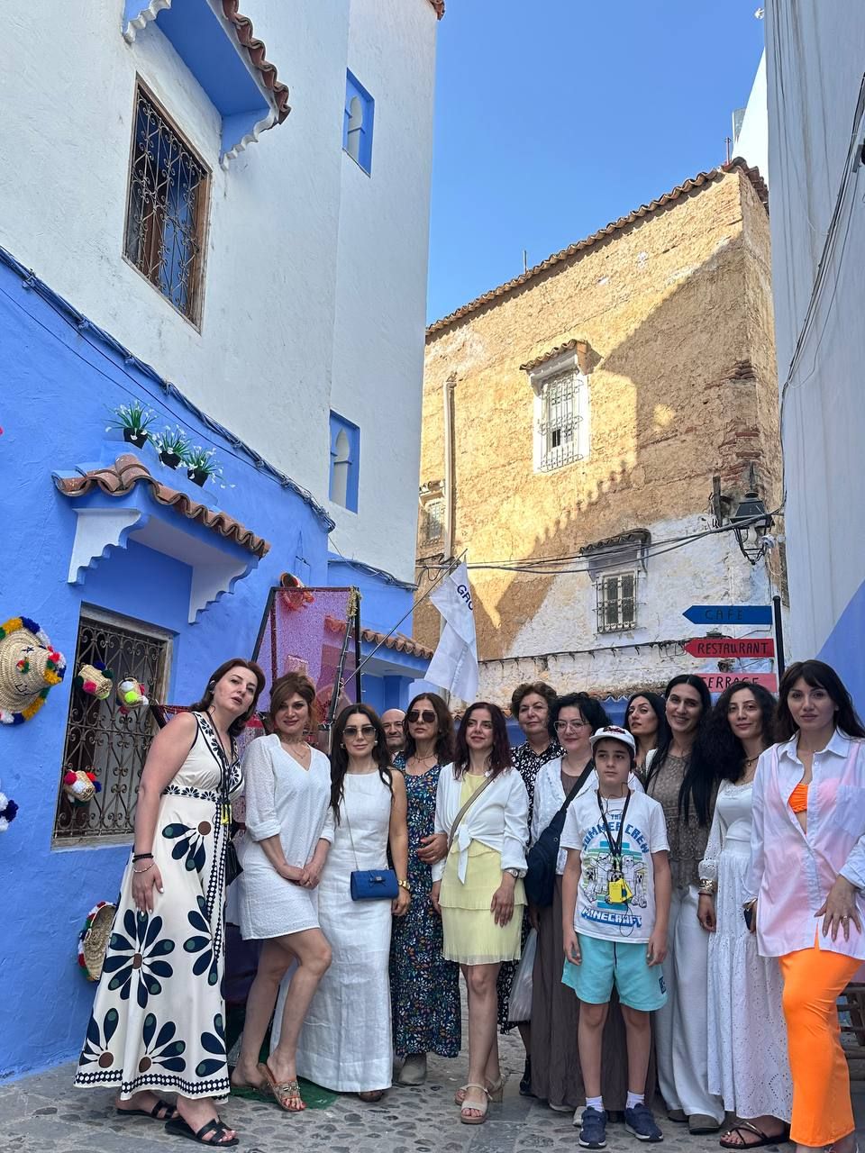 Un groupe de personnes posant dans une rue étroite, avec des bâtiments peints en bleu et en blanc.