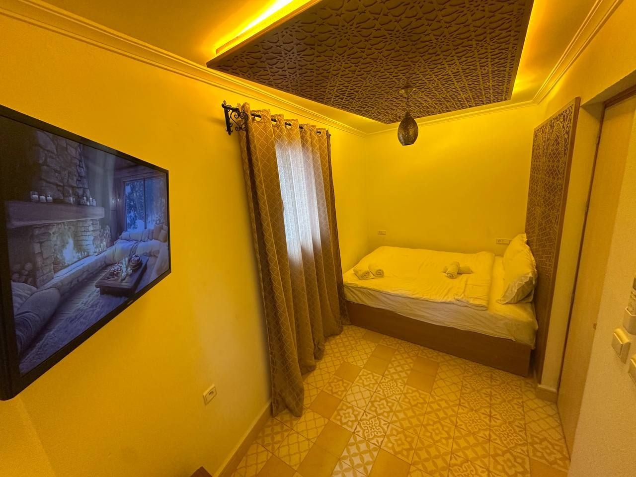 Una habitación con una cama, un televisor montado en la pared y suelo con baldosas estampadas.