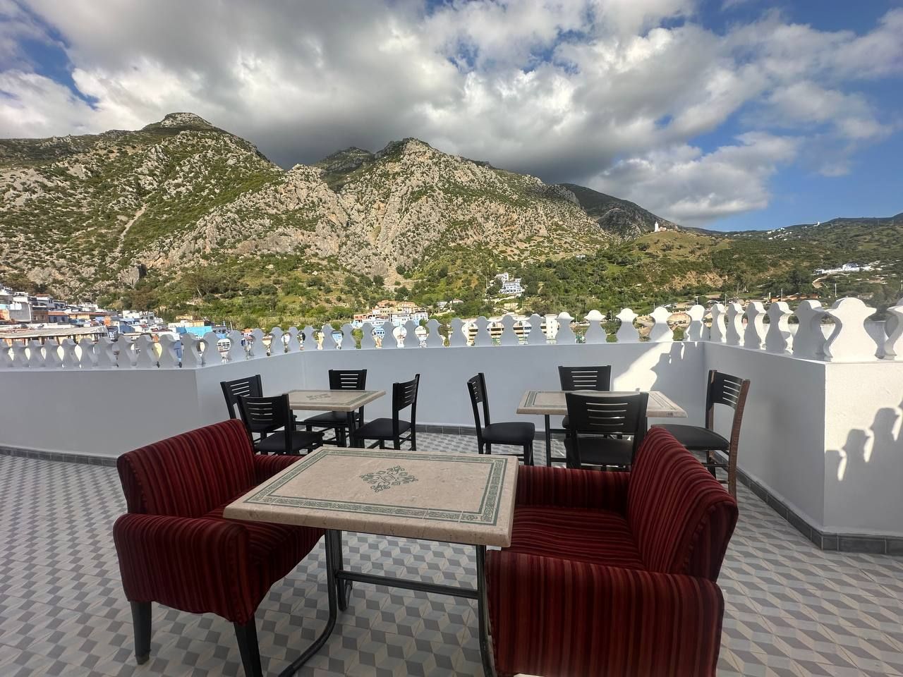 An outdoor terrace with tables and chairs, overlooking a mountainous landscape.