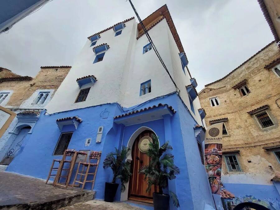 Un edificio con fachada azul, puerta de madera y un letrero que dice "MARHABA".