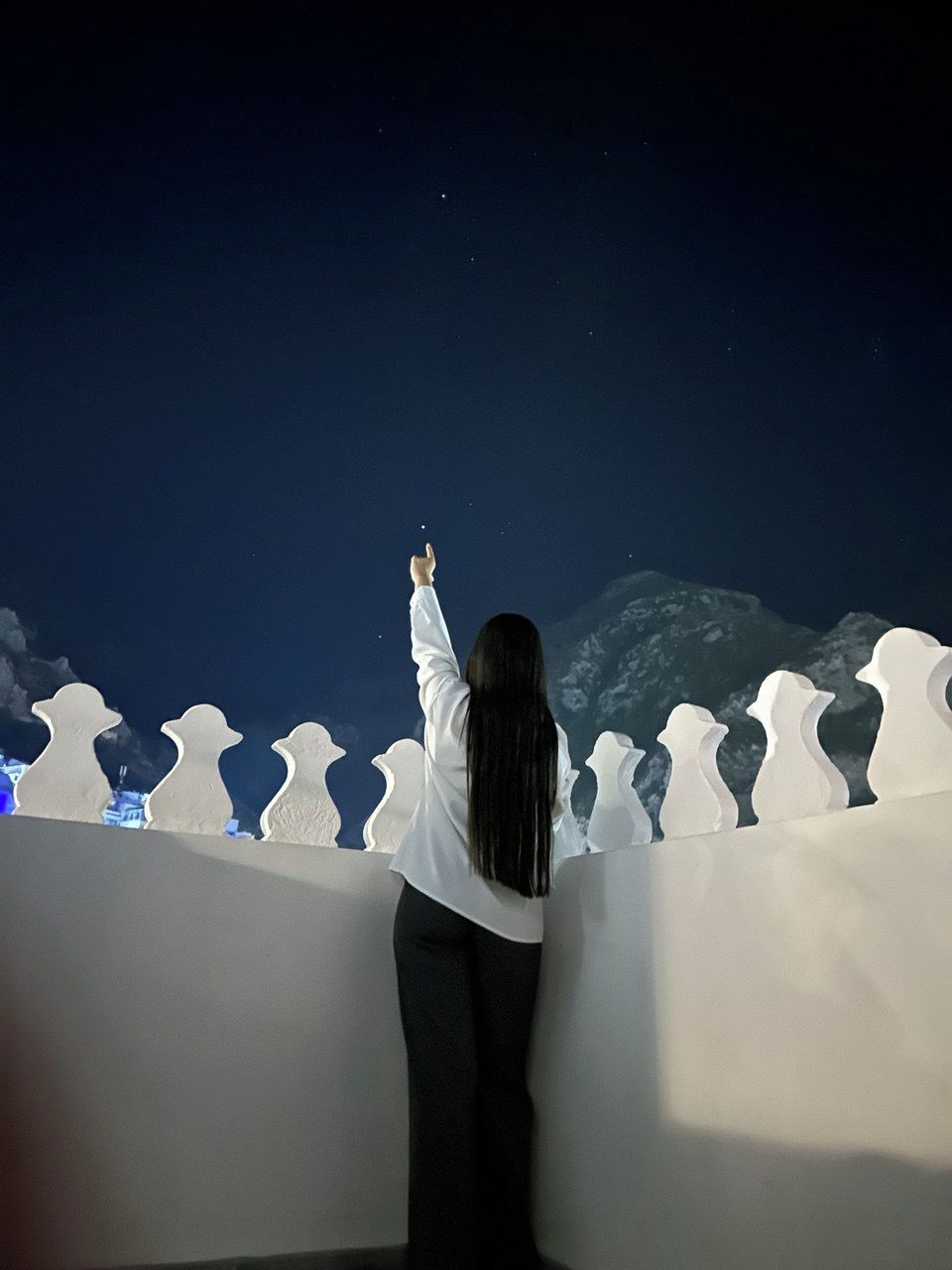 Une personne se tient sur un balcon, d’où l’on peut admirer une montagne et le ciel.