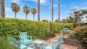 A patio area with light blue Adirondack chairs and a picnic table, surrounded by well-maintained hedges and palm trees. - San Diego Surf Shack #3 -1/2 Block to the Pacific! (San Diego)