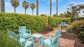 Un espace patio avec des chaises Adirondack bleu clair et une table de pique-nique, entouré d’une haie bien entretenue et de palmiers.