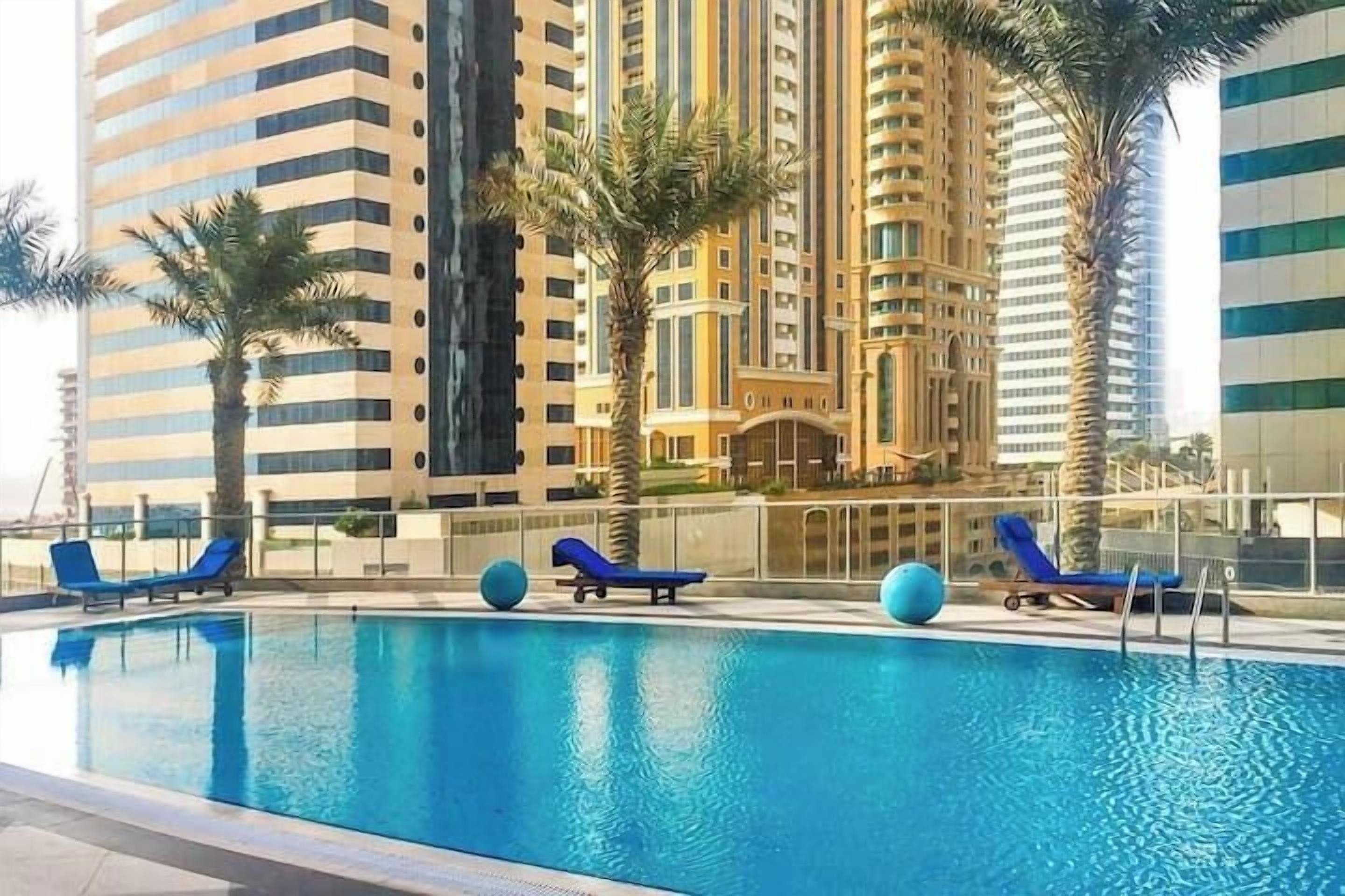 A swimming pool with lounge chairs and palm trees.