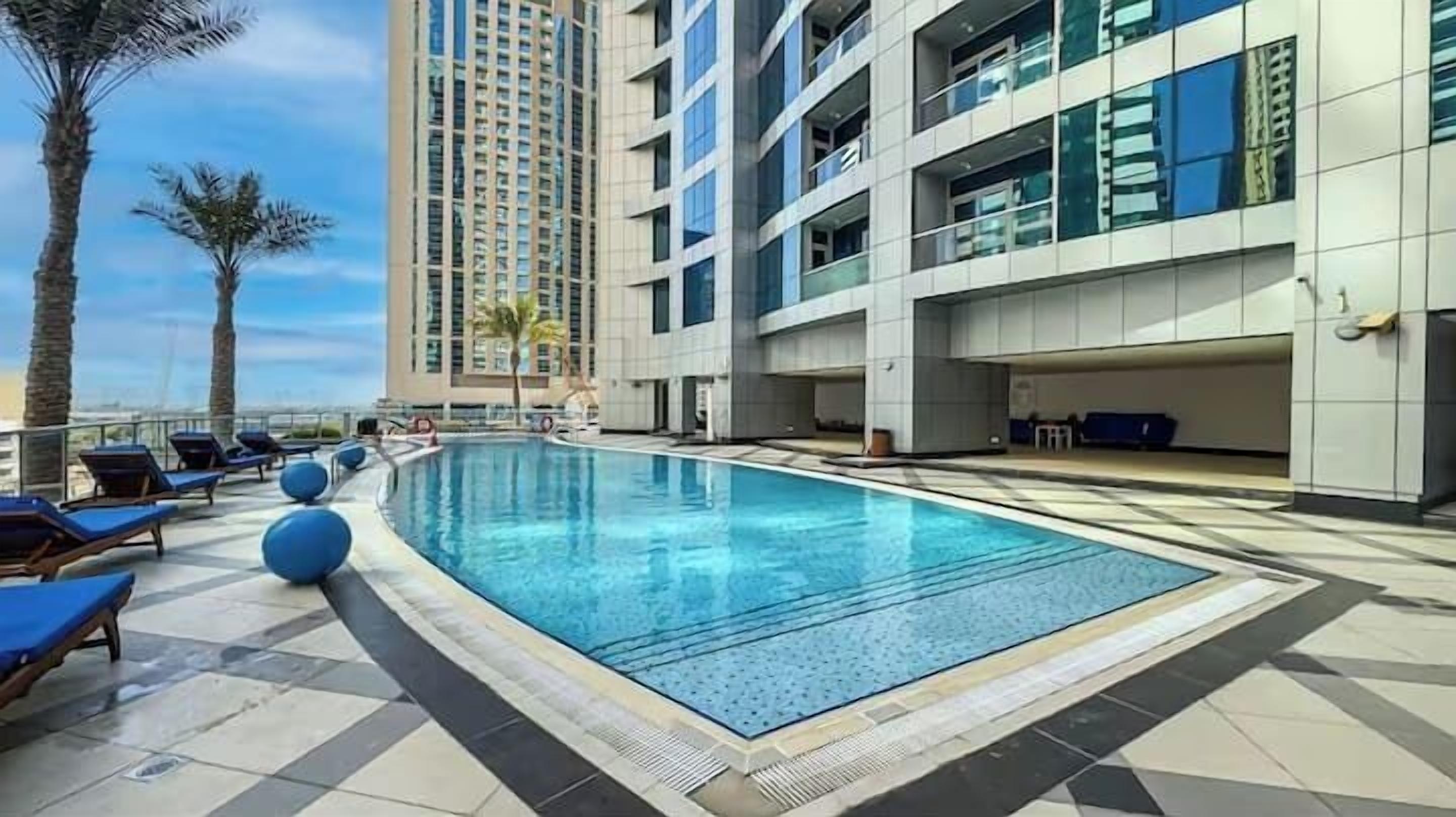 A swimming pool with lounge chairs, a tall building, and palm trees.