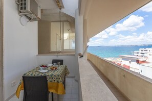 Un balcon avec une table dressée pour deux personnes, donnant sur une étendue d’eau et sur des bâtiments.