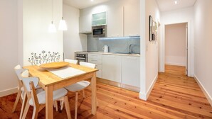 A modern kitchen with white cabinets, a wooden dining table, and pendant lights. - GuestReady – Homely Base Near Castle (Lisbon)