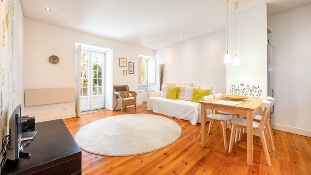 A modern living room with a wooden floor, white sofa, dining table, and a TV on a stand. - GuestReady – Homely Base Near Castle (Lisbon)