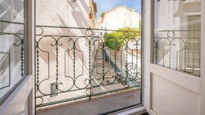 A balcony with a wrought iron railing, a view of a narrow street with buildings, and a staircase leading down. - GuestReady – Homely Base Near Castle (Lisbon)