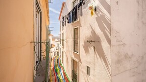 A narrow street with buildings on either side, featuring balconies with clothes drying and a colorful flag. - GuestReady – Homely Base Near Castle (Lisbon)