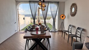 A dining area with a table set for four, a floor lamp, and a view of the landscape through large windows.