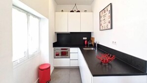 A modern kitchen with white cabinets, a black countertop, and a red trash bin. - Lovely and Modern 1 Bedroom City Centre Cannes (Cannes)