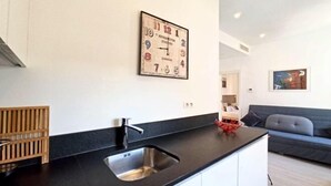 A modern kitchen with a black countertop, stainless steel sink, and a framed clock on the wall. - Lovely and Modern 1 Bedroom City Centre Cannes (Cannes)