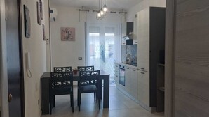 Una cocina moderna con armarios de colores claros, un comedor con sillas negras y un refrigerador visible.