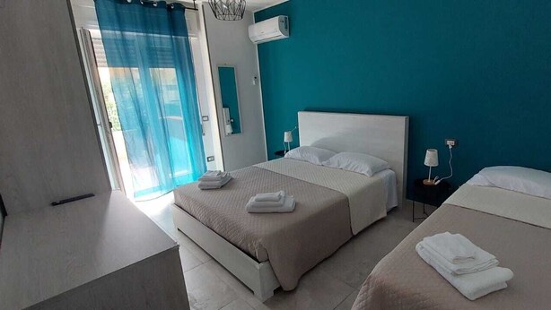 Habitación de hotel con dos camas, un ventanal grande con cortinas azules y un equipo moderno de aire acondicionado en la pared.