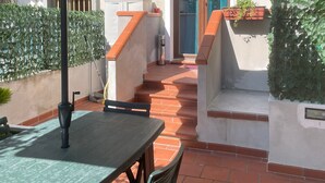 Un patio con mesa y sillas bajo un paraguas verde, una escalera y plantas en macetas.