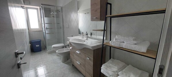A modern bathroom with a glass shower enclosure, a sink, a toilet, and a towel rack. - Numa Apartment Sardinia (Monserrato)