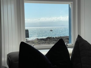 A room with a view of the sea through a window, a chair, and two pillows.