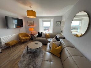 A modern living room with a sofa, armchair, coffee table, and a TV mounted on the wall.