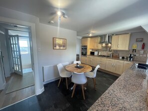 A modern kitchen with a dining area, featuring a round table, white chairs, and wooden cabinets. - Forth, seaside 3 bed apartment, stunning views, convenient, central location , (Pittenweem)