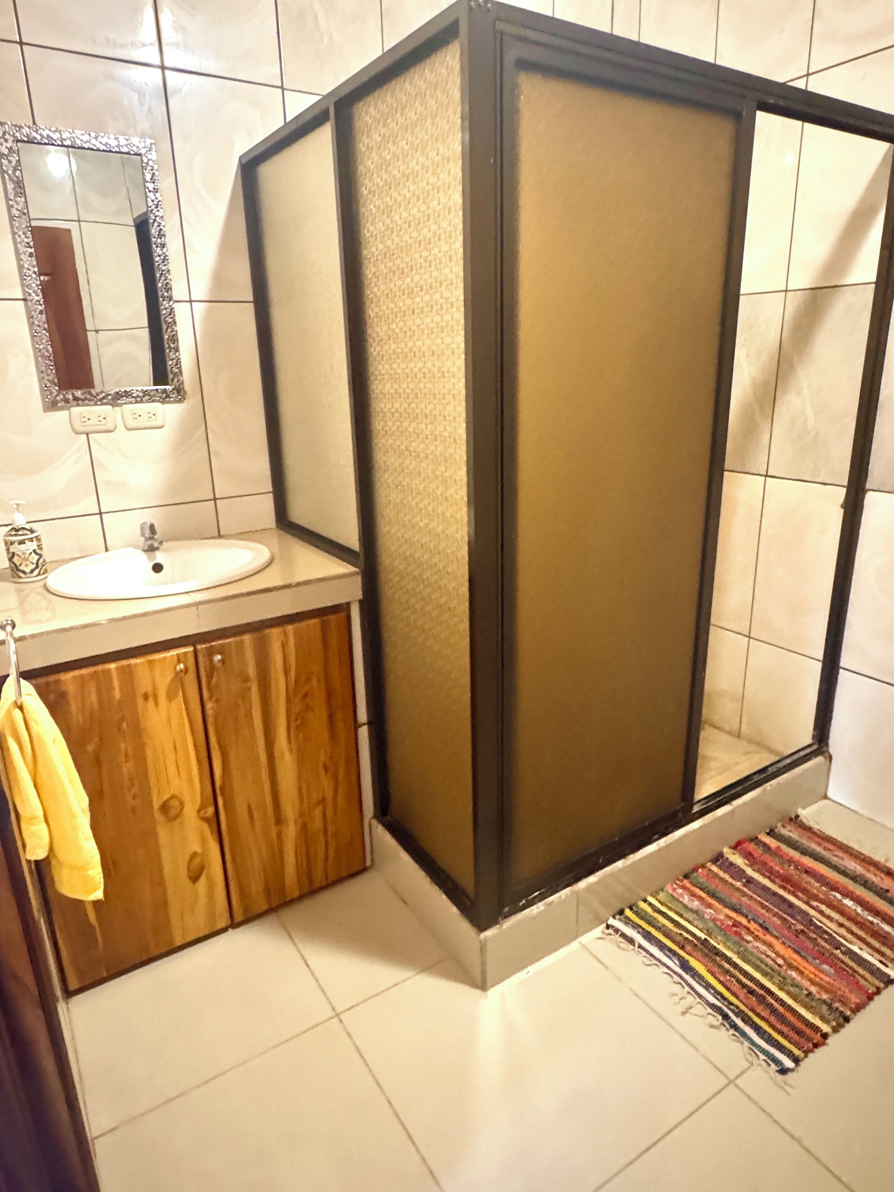 Un baño con tocador de madera, lavamanos, espejo y cabina de ducha.