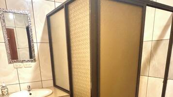 Un baño con tocador de madera, lavamanos, espejo y cabina de ducha.