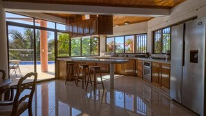 Une cuisine spacieuse dotée d’un îlot central, de meubles en bois et de grandes fenêtres offrant une vue sur l’extérieur.