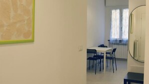 Un coin repas avec une table blanche et des chaises bleues, un tableau encadré de vert accroché au mur, et un miroir rond sur la droite.