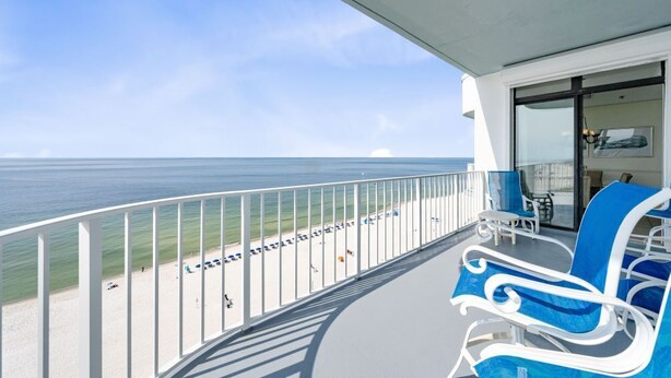 A balcony with a view of the ocean, white railings, and blue lounge chairs.