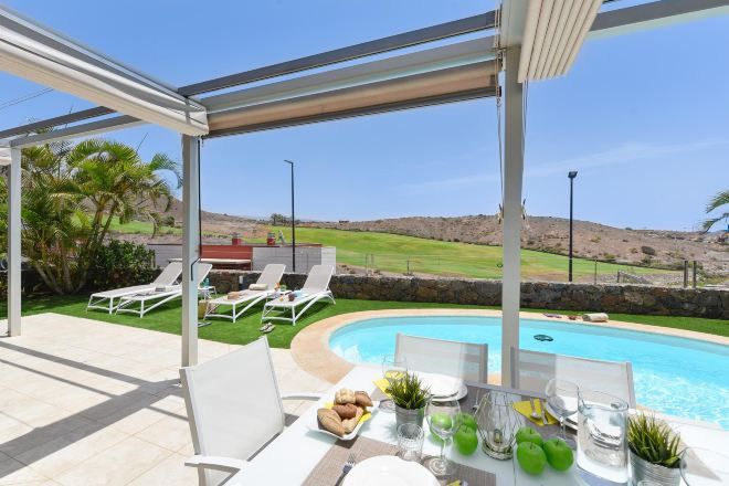 Ein überdachter Außenbereich mit Pool, Liegestühlen und einem Esstisch.