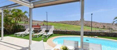 Un espacio al aire libre techado con piscina, sillas de descanso y una mesa lista para comer.