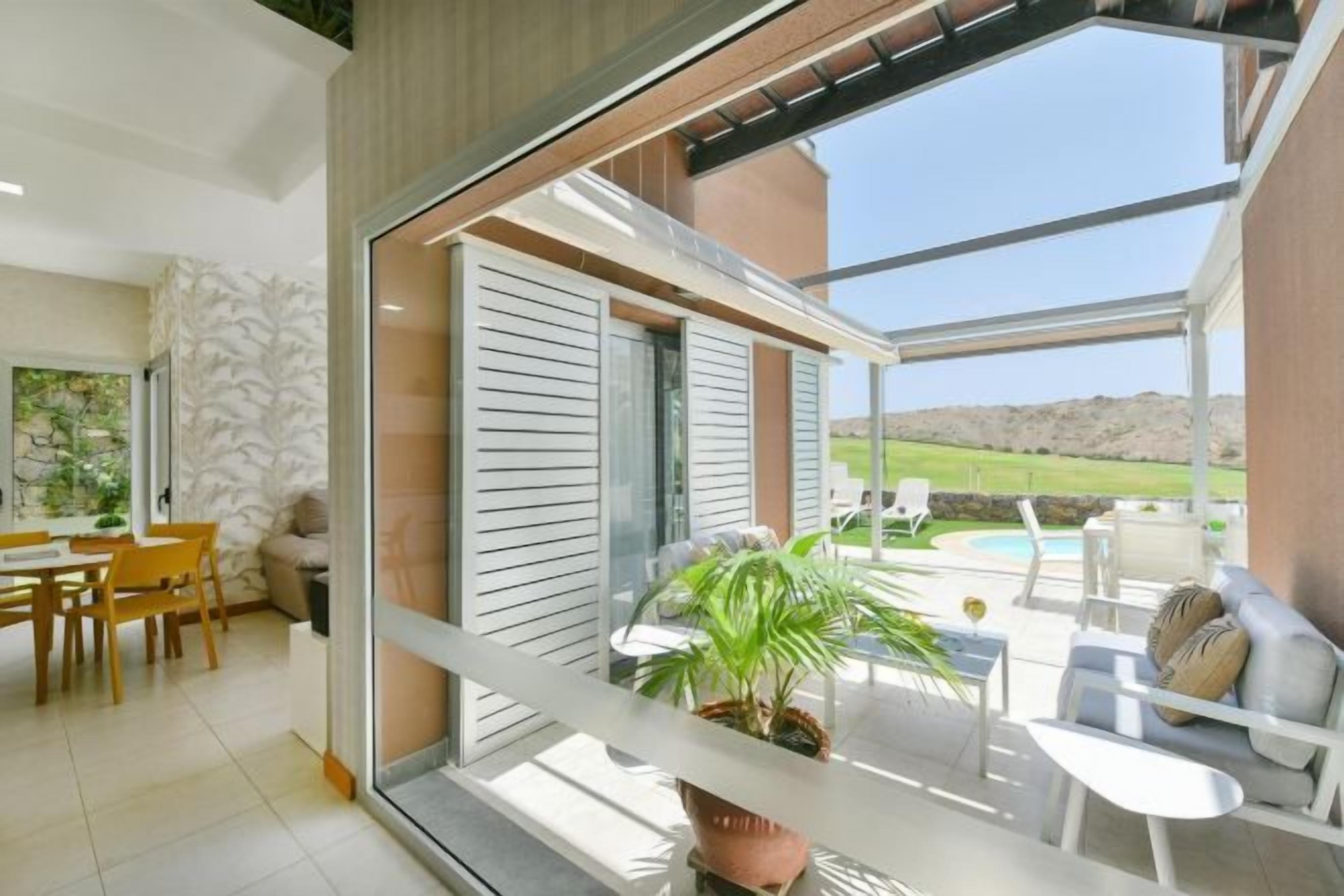 A modern interior with a dining area, a balcony with outdoor seating, and a view of a swimming pool.