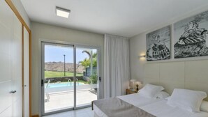 A bedroom with a large bed, a sliding glass door to a pool area, and two wall-mounted paintings. - Vista Golf 10 Salobre by VillaGranCanaria (Comarca Sur)