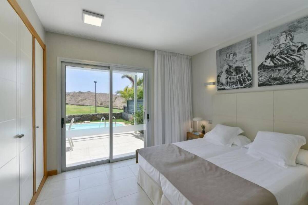 A bedroom with a large bed, a sliding glass door to a pool area, and two wall-mounted paintings.