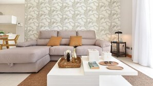 A modern living room with a sectional sofa, a coffee table with decorative items, and a patterned wallpaper. - Vista Golf 10 Salobre by VillaGranCanaria (Comarca Sur)