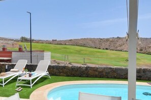 Un espace piscine avec des chaises longues, un mur en pierre et une vue sur un terrain de golf.