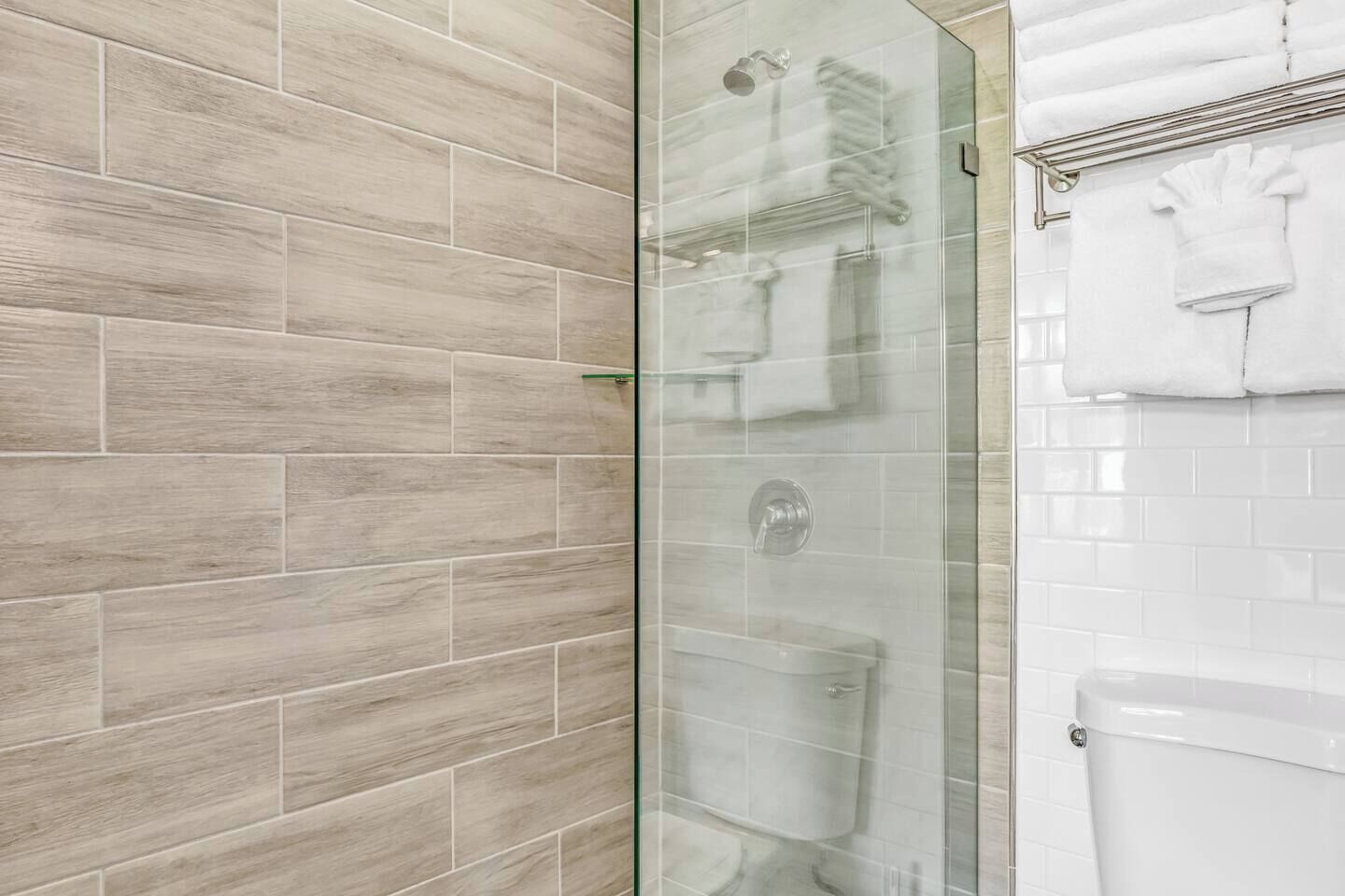 A bathroom with a glass shower enclosure, a toilet, and a towel rack.