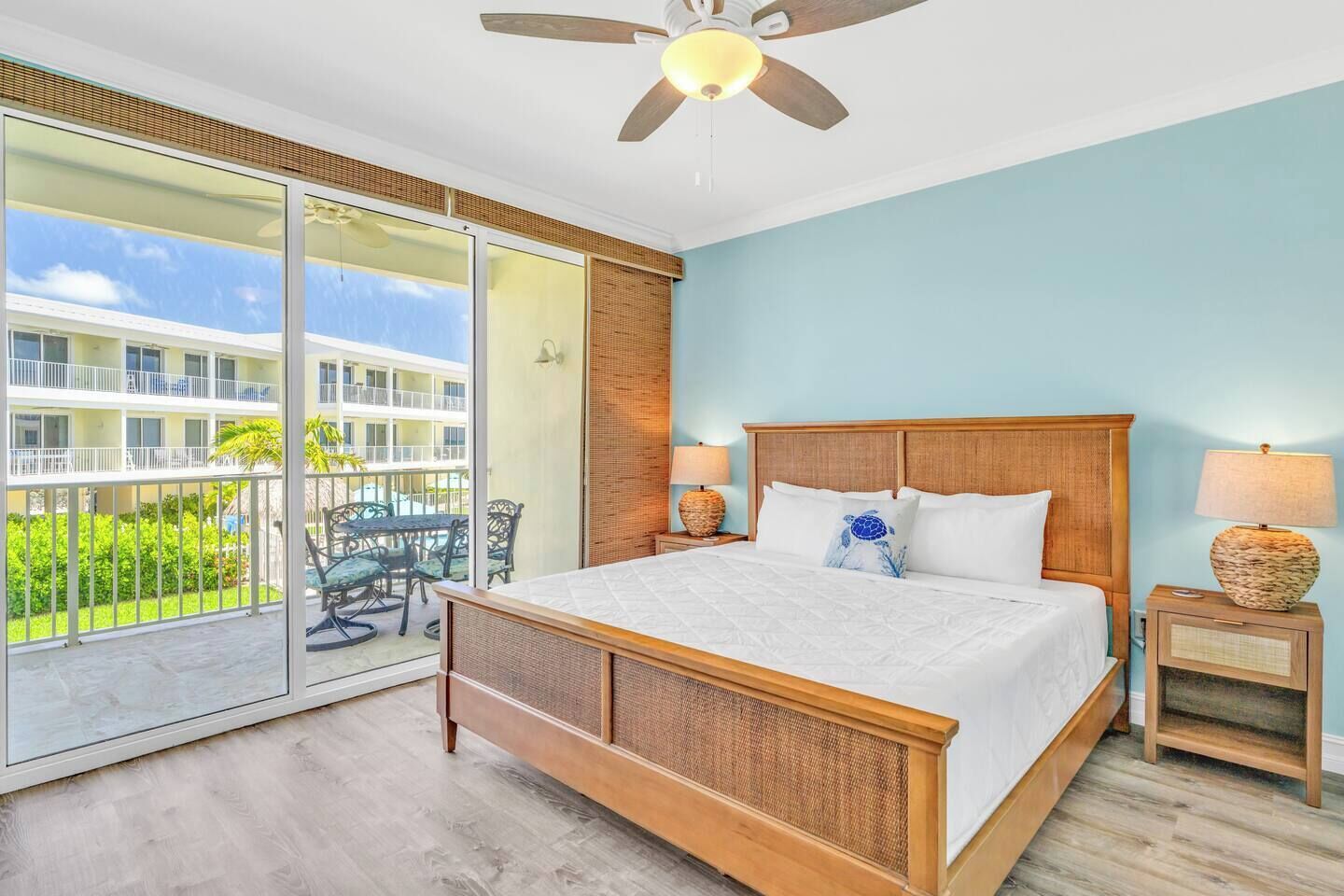 A spacious bedroom with a large bed, a ceiling fan, and a view of a building through a sliding glass door.